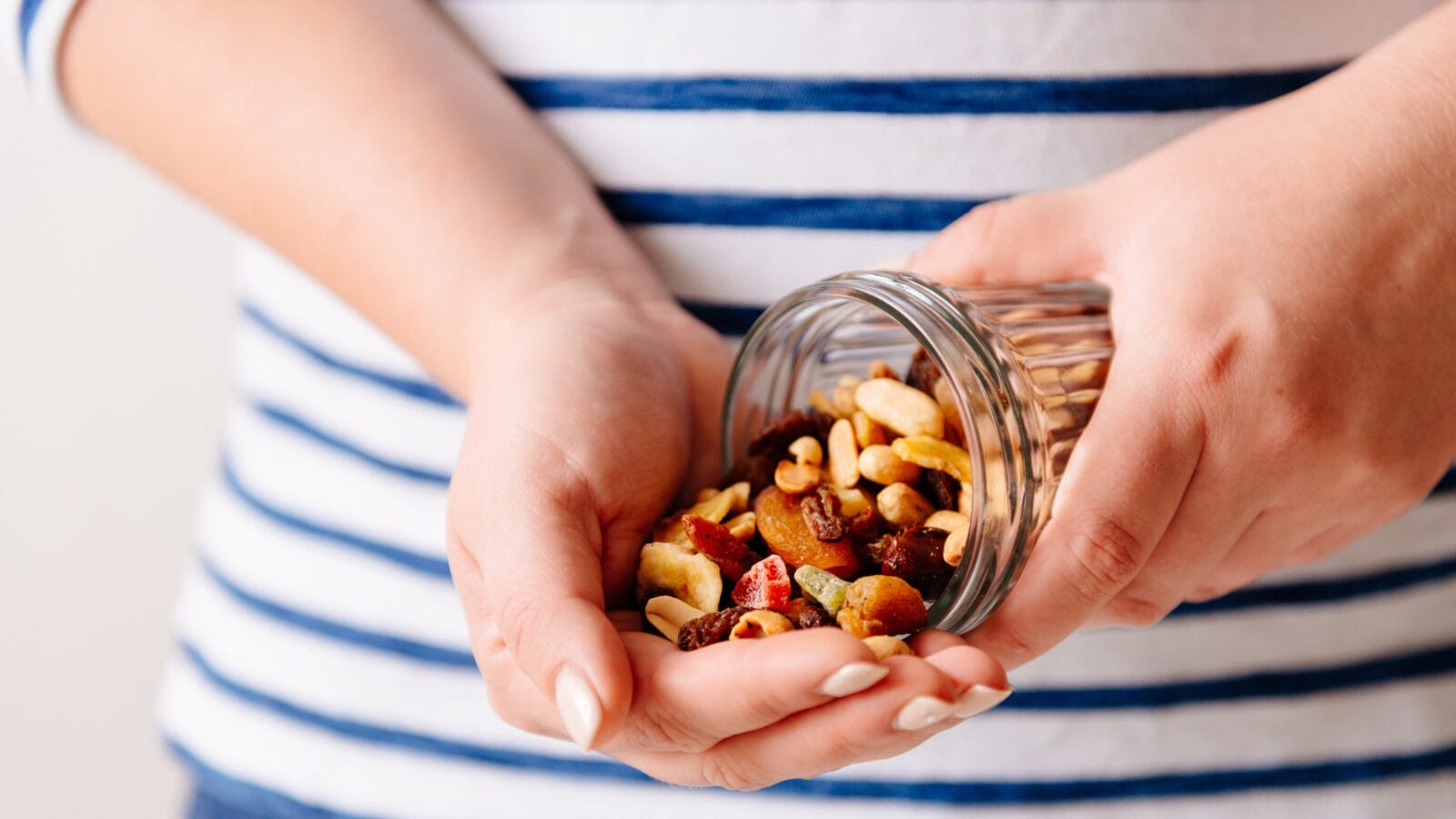 Hands holding a jar of nuts and dried fruits.