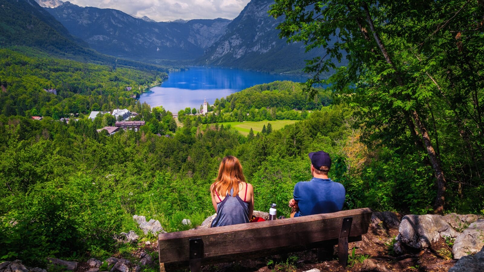 Wonderful hiking place with cheerful hiker couple on the bench enjoying the view from the hill, lake Bohinj, Slovenia, Europe