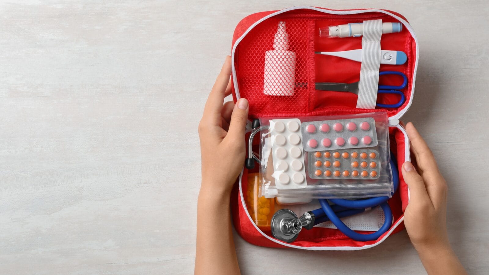 Hands holding first aid kit on white wooden table, top view.