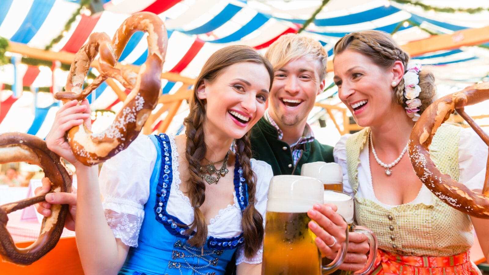 Three friends in beer tent at Dult or Oktoberfest holding giant pretzels up in the air