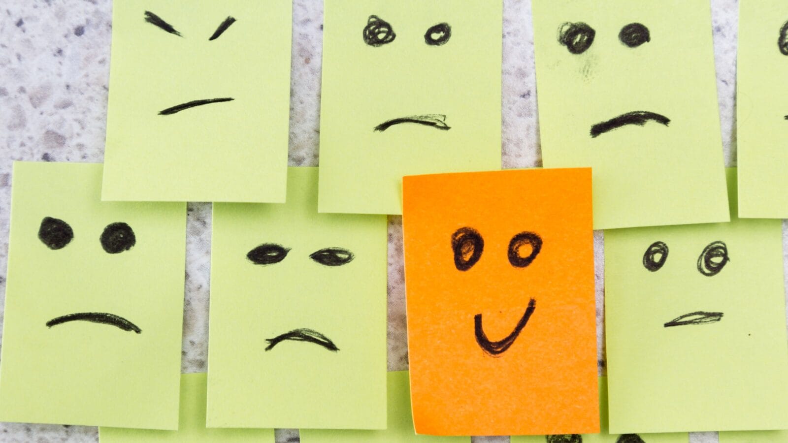 Concept for a positive attitude with small office notes with multiple faces and one that stands out with a smile