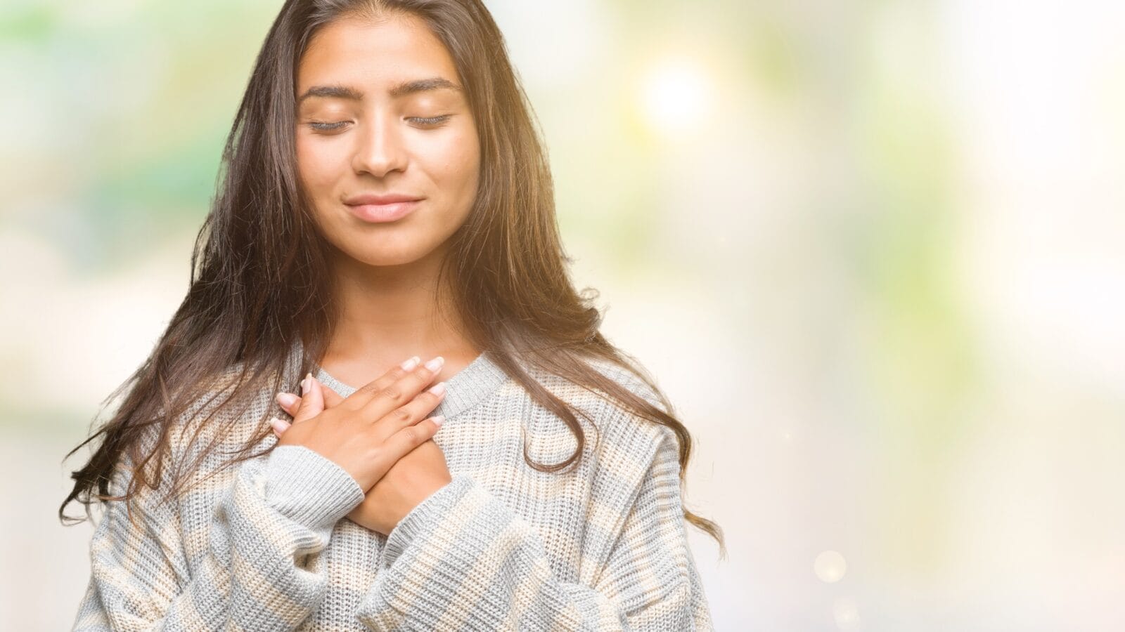 Young woman smiling with hands on chest and closed eyes, showing grateful gesture on face.