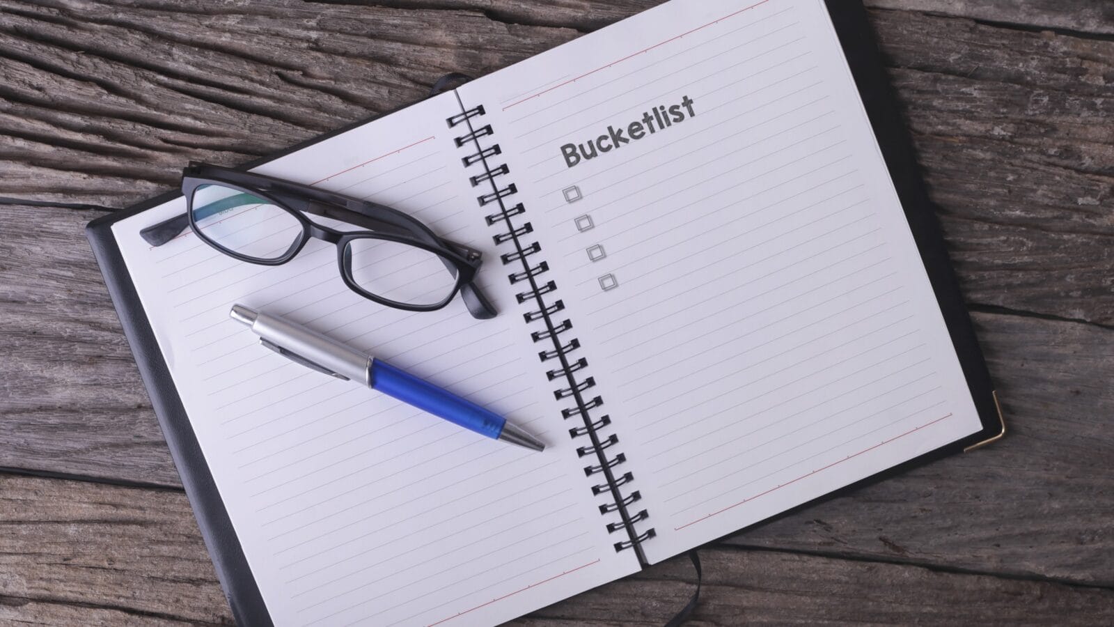 Conceptual,notebook on a wooden table. open diary, glasses and pen with Bucketlist word
