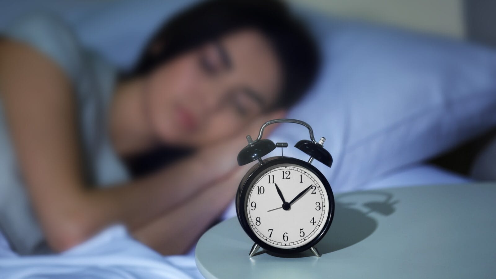 Young woman sleeping in bed with alarm at night