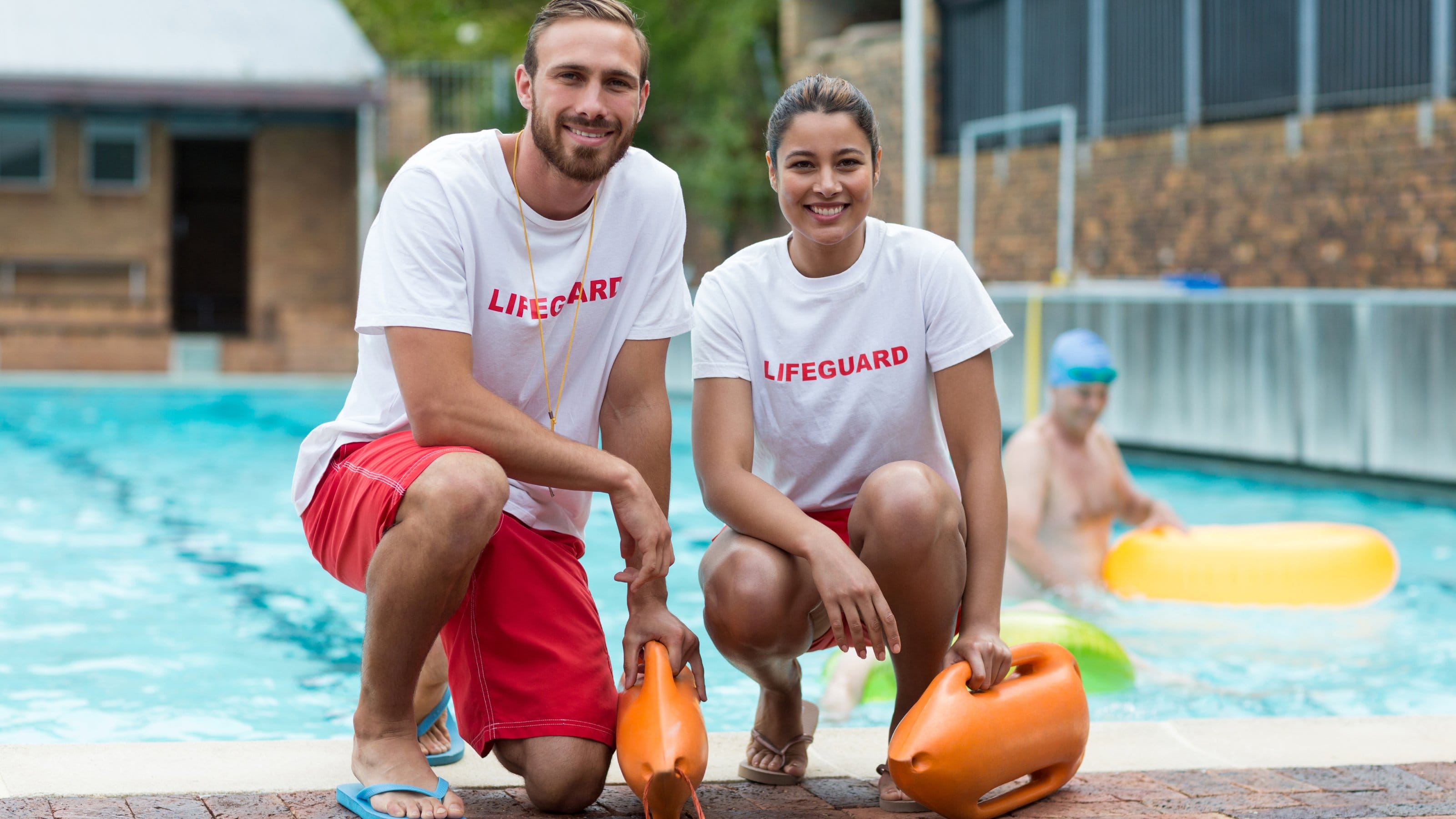 Portrait of male and female lifeguards holding rescue cans at poolside