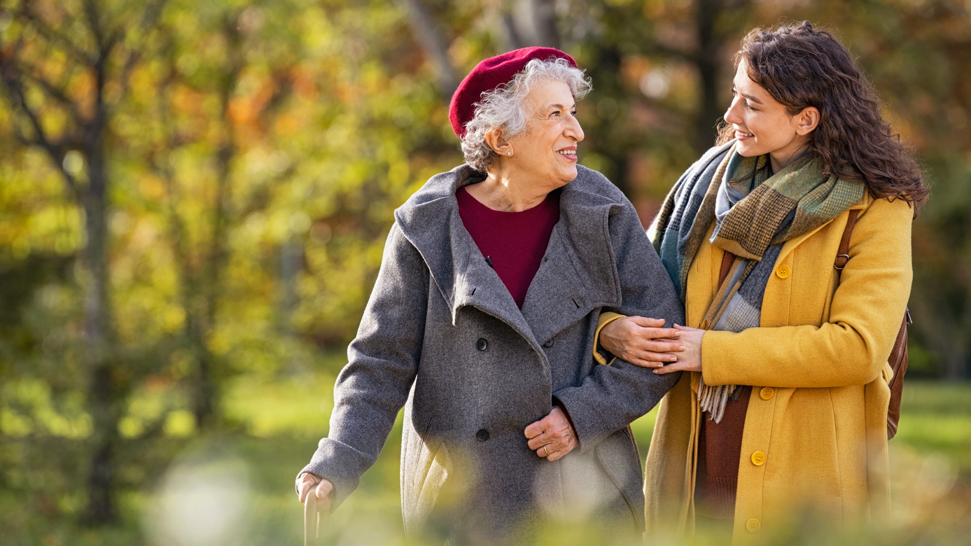 Smiling lovely caregiver and senior lady walking in park
