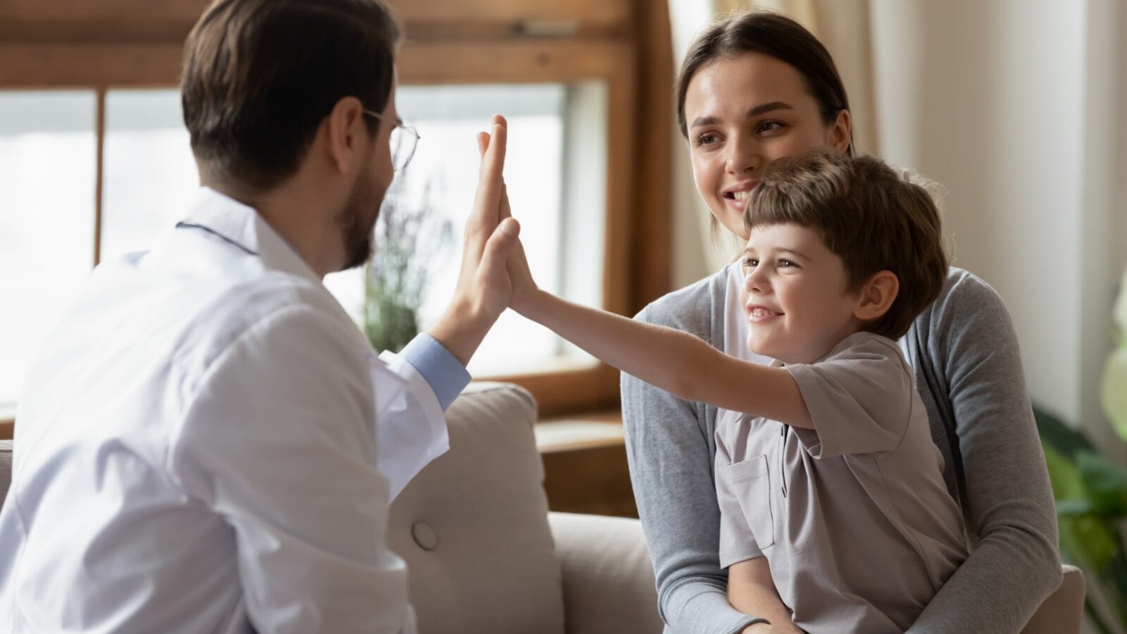 Happy little boy with his mom giving a high five to a doctor.
