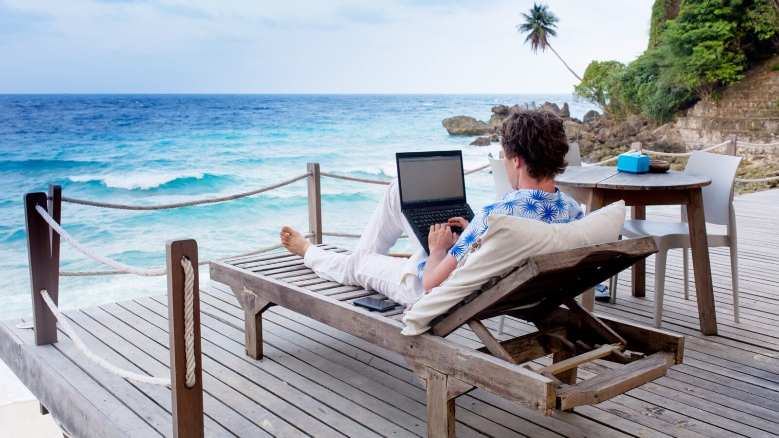 man with laptop and mobile phone running remotely on colorful beach of island
