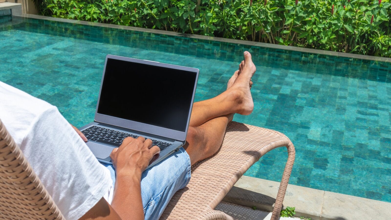 Man with laptop on a pool lounge chair