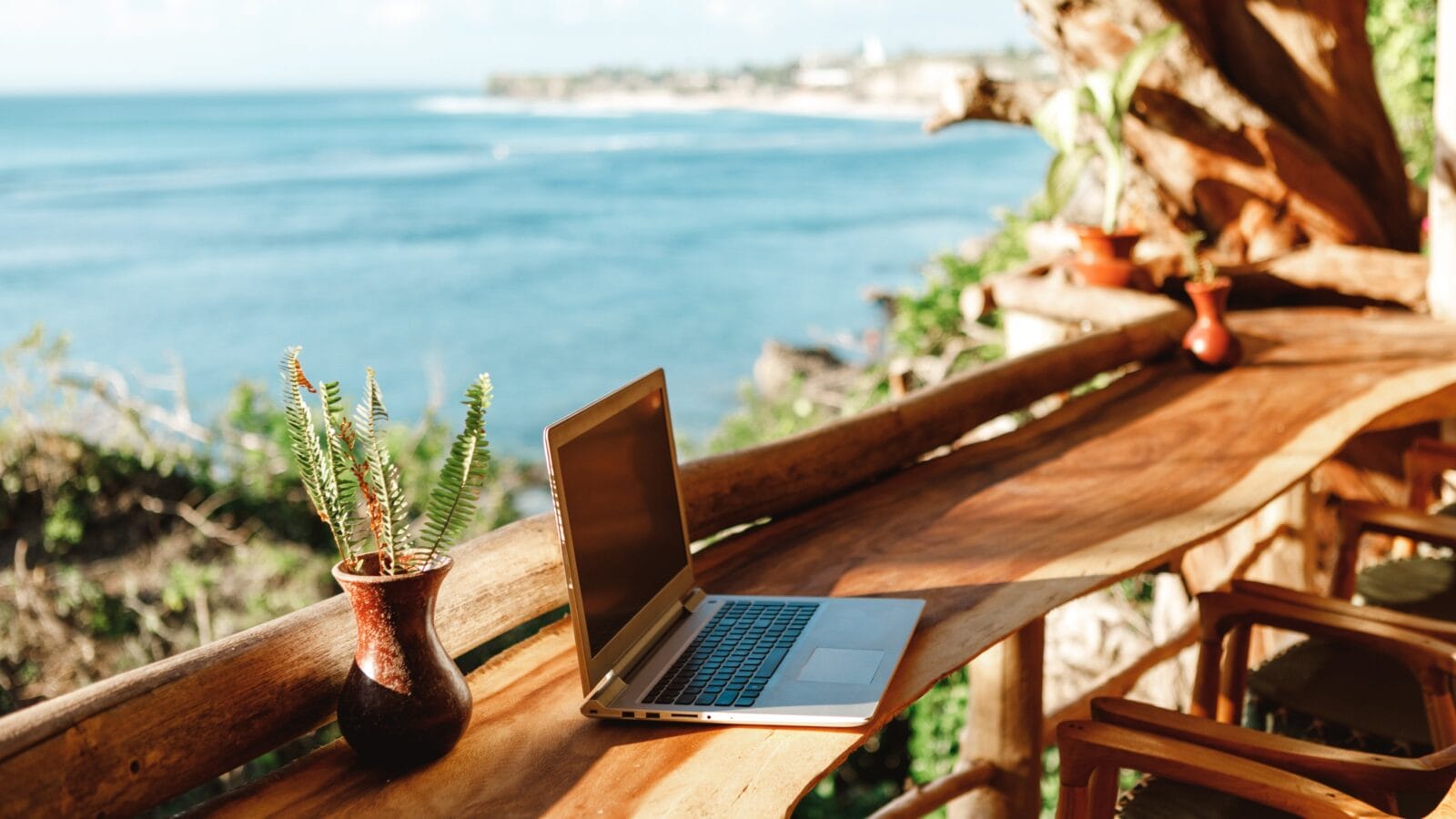 Open laptop with black screen on wooden table work space outdoors with amazing view on the ocean.