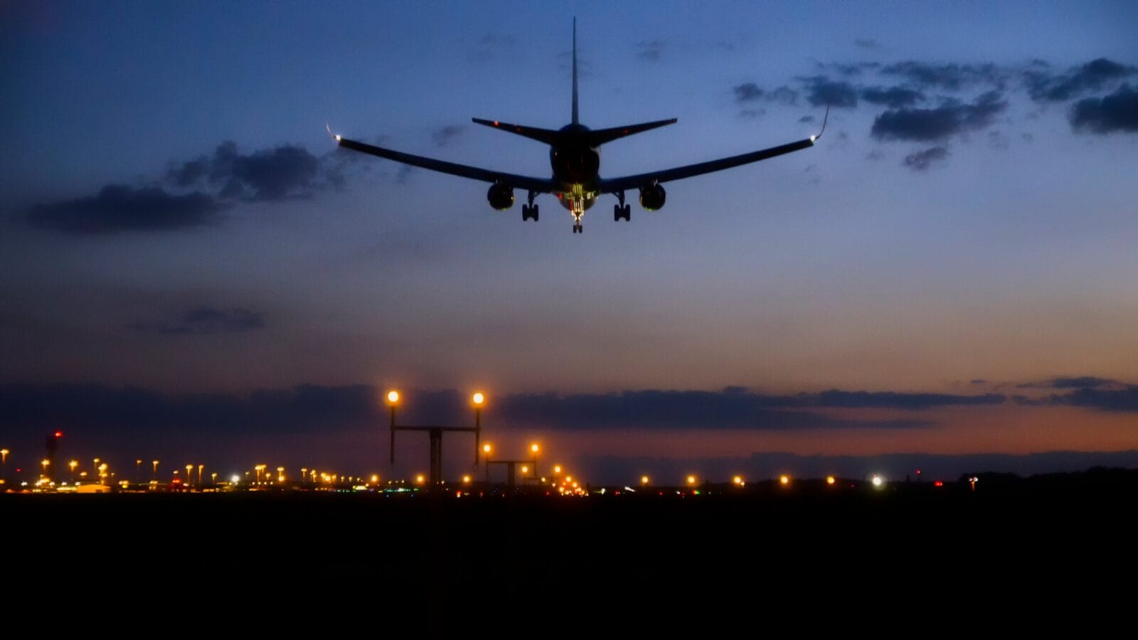 Commercial airliner landing above lighten up approach lights of international airport runway