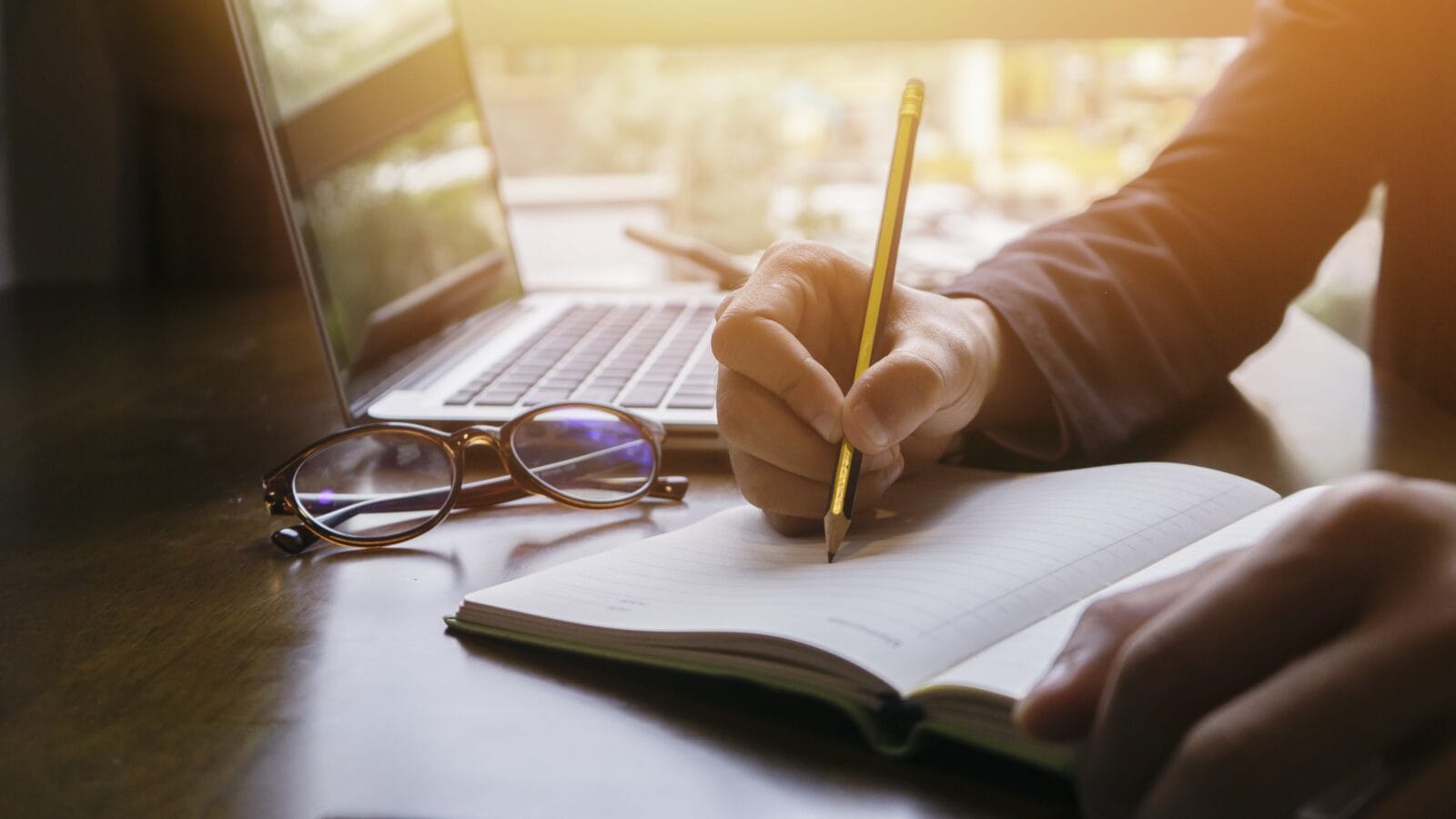 A person writing with a pencil on a paper notebook.