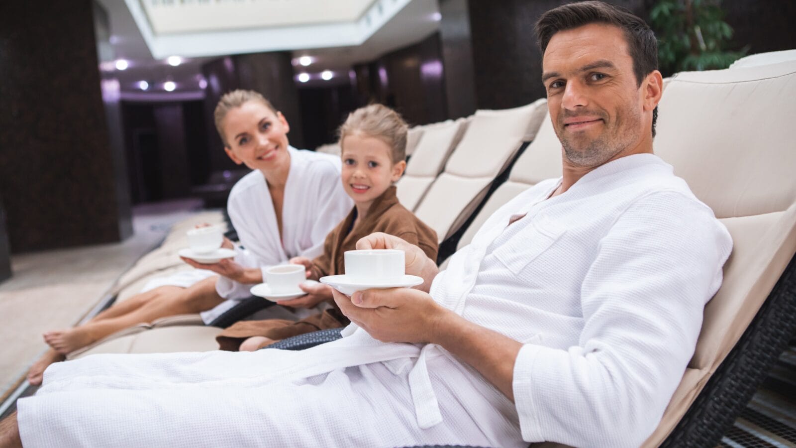 Waist up portrait of delighted man and woman sitting in a Spa on deckchairs with kid.