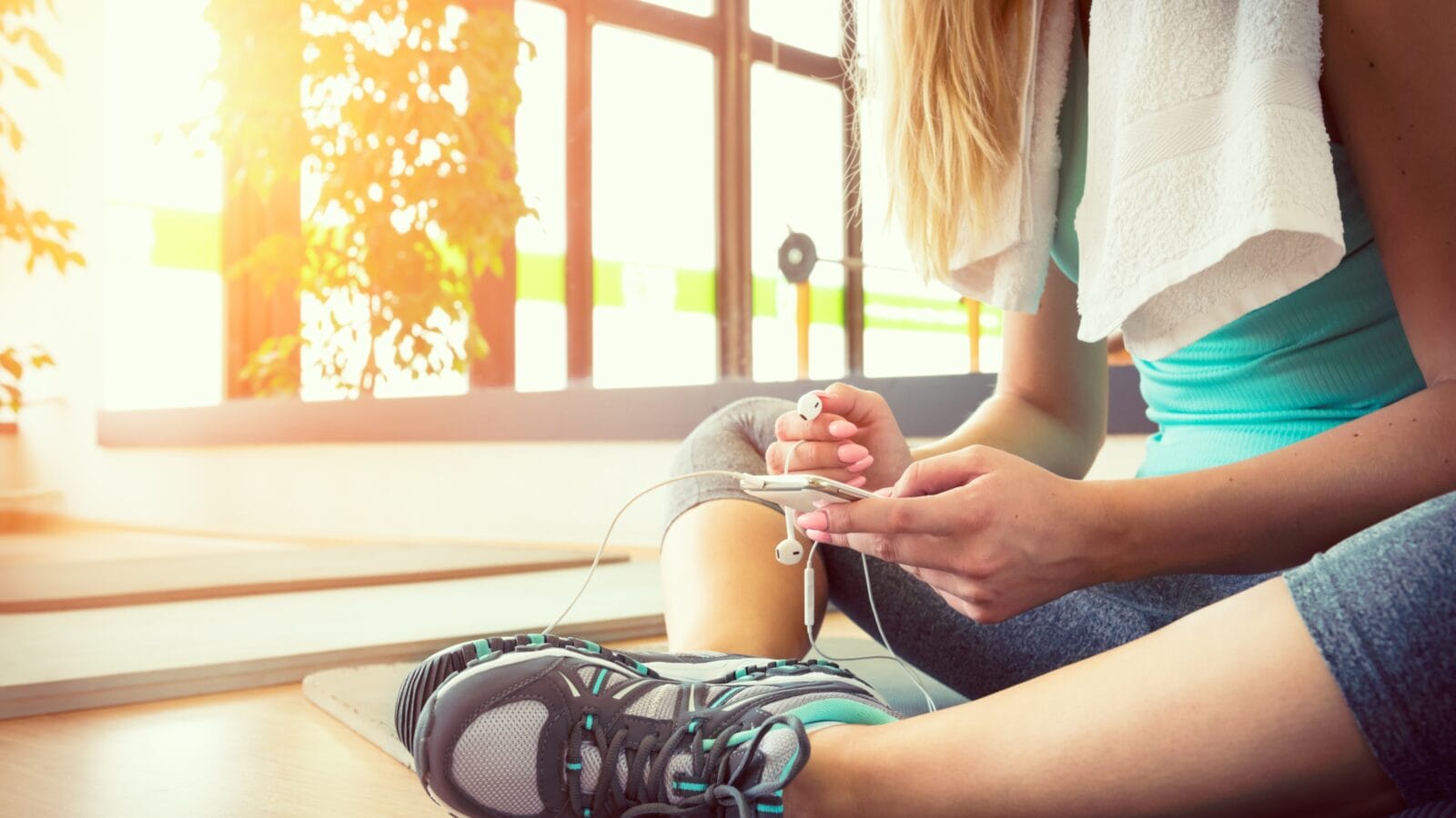 Attractive blond woman with smart phone, resting during workout.