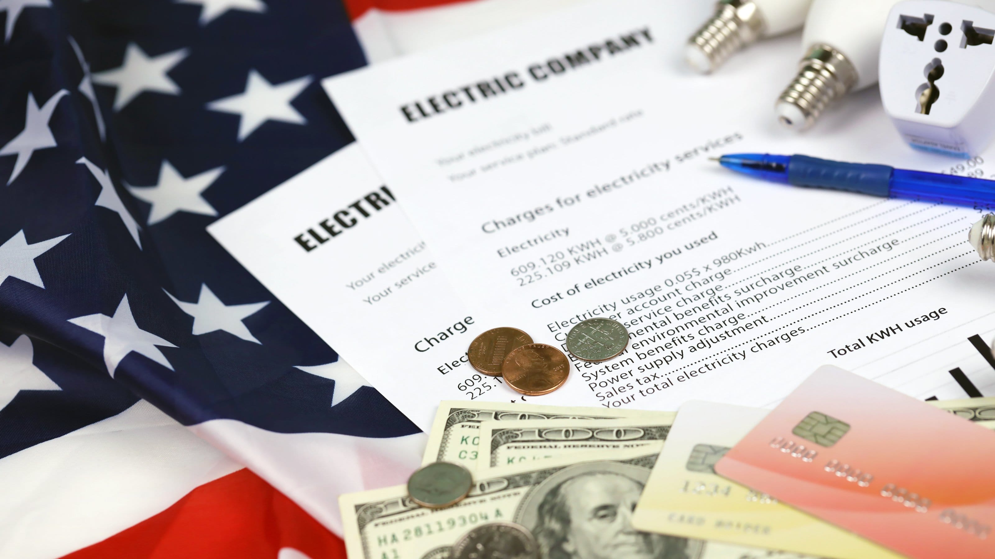 Electric bills with money lightbulbs and american flag beside them.