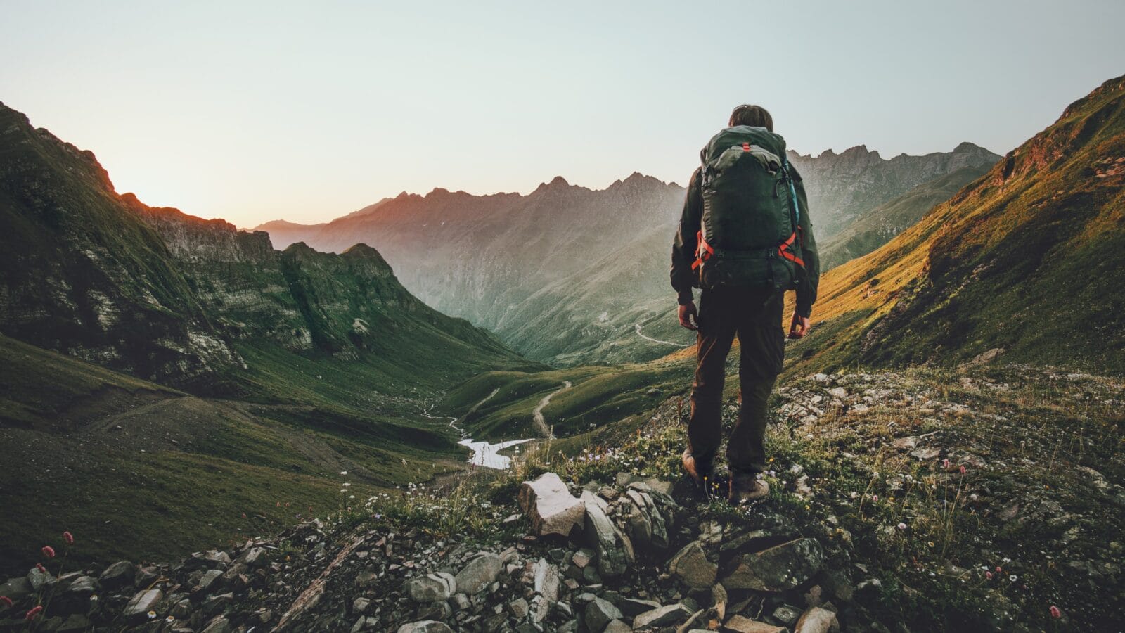 Man hiking at sunset mountains with a backpack.