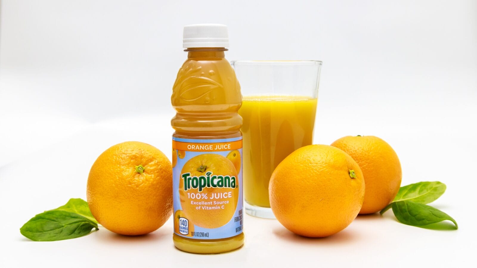 Citrus juice from Tropicana with glass filled with juice and oranges around.