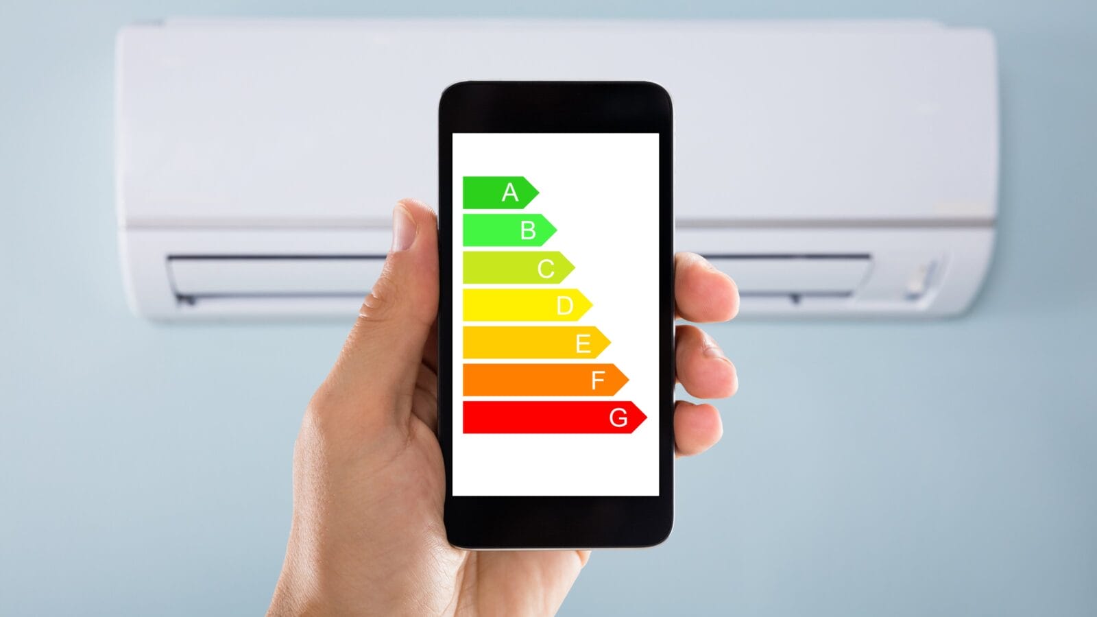 Closeup of man's hand using energy label on mobile phone against air conditioner