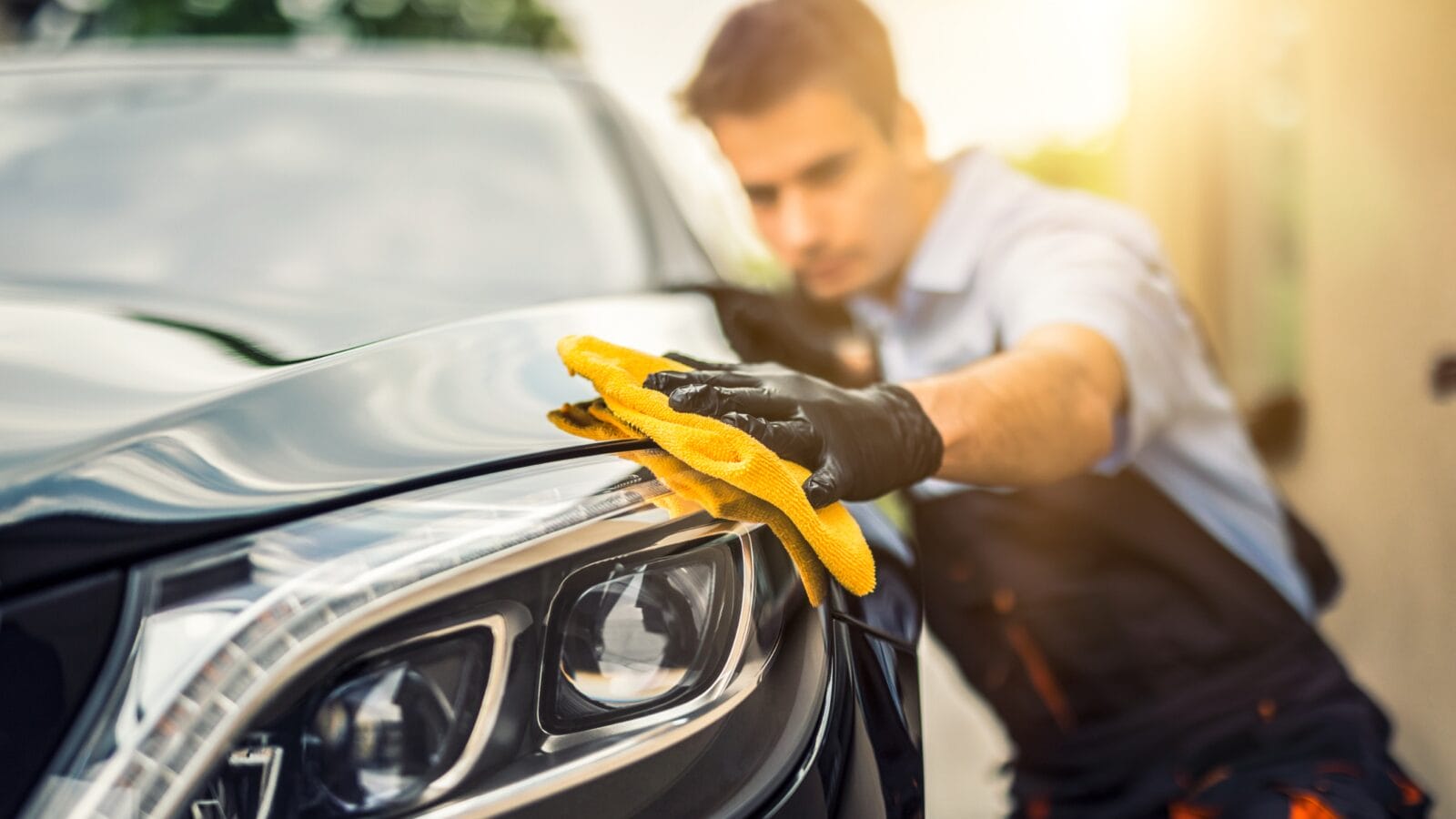 A man holding microfiber in hand and polishing a car.