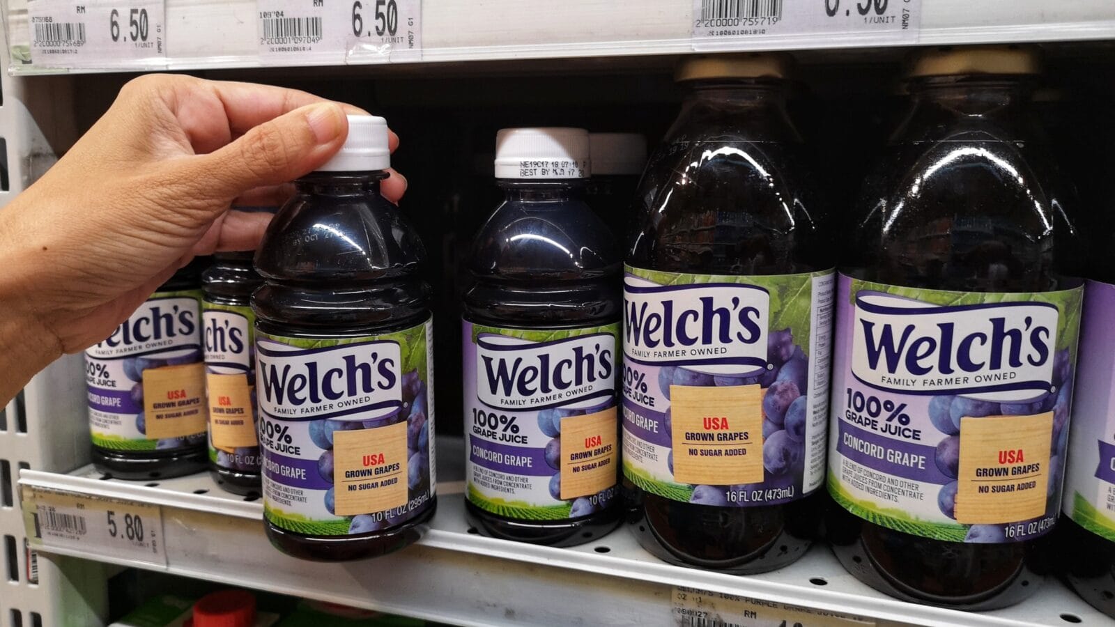 Upclose a hand are buying plastic bottle of Welch's brand 100% white grape juice in a supermarket aisle.
