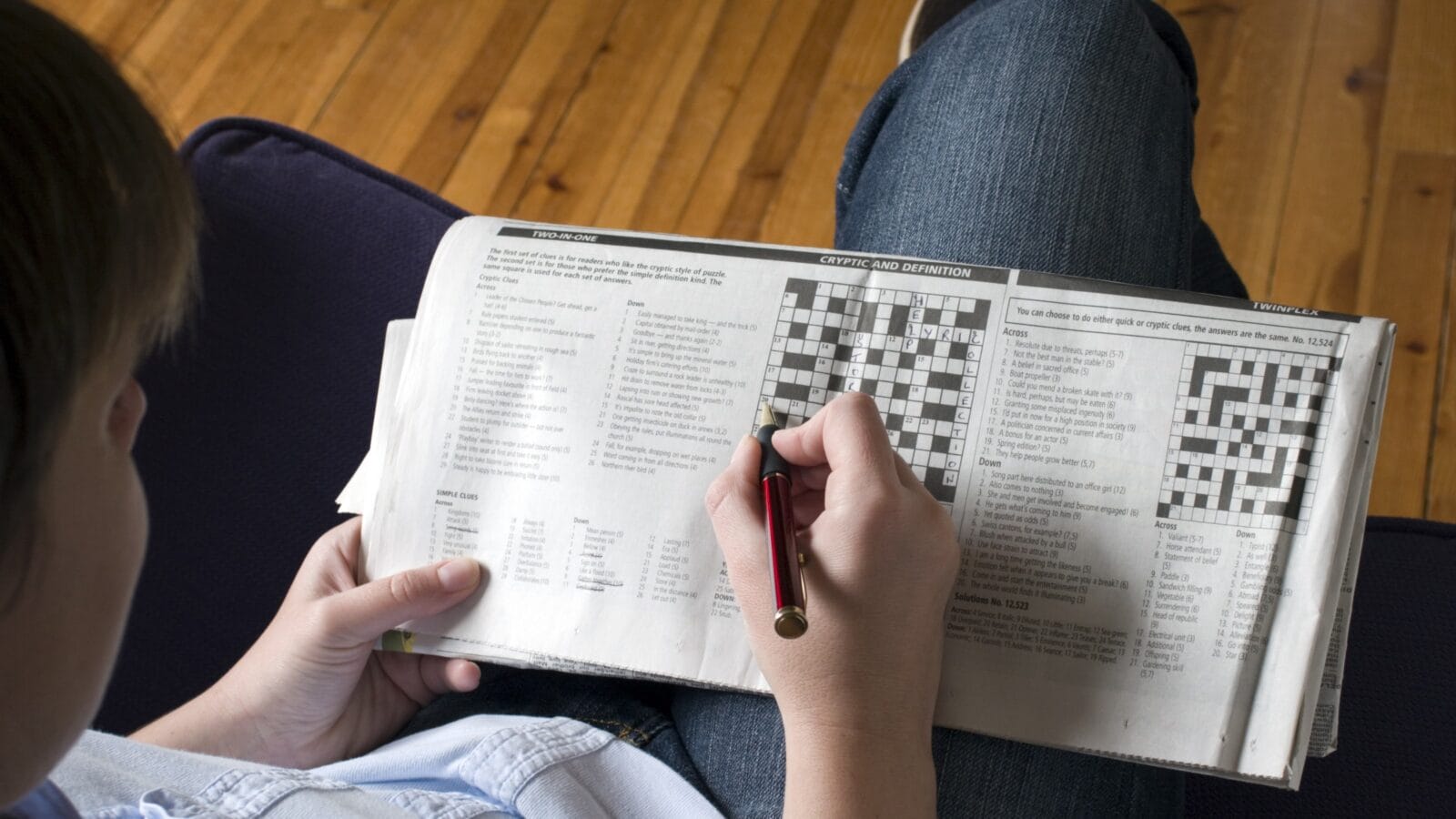 A lady sitting on a sofa doing the crossword.