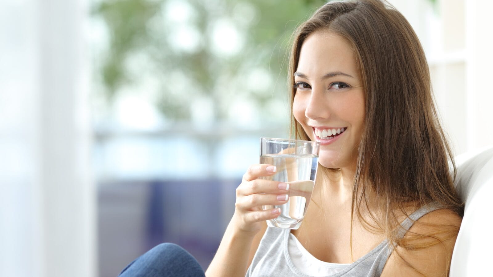 Girl drinking water sitting on a couch.