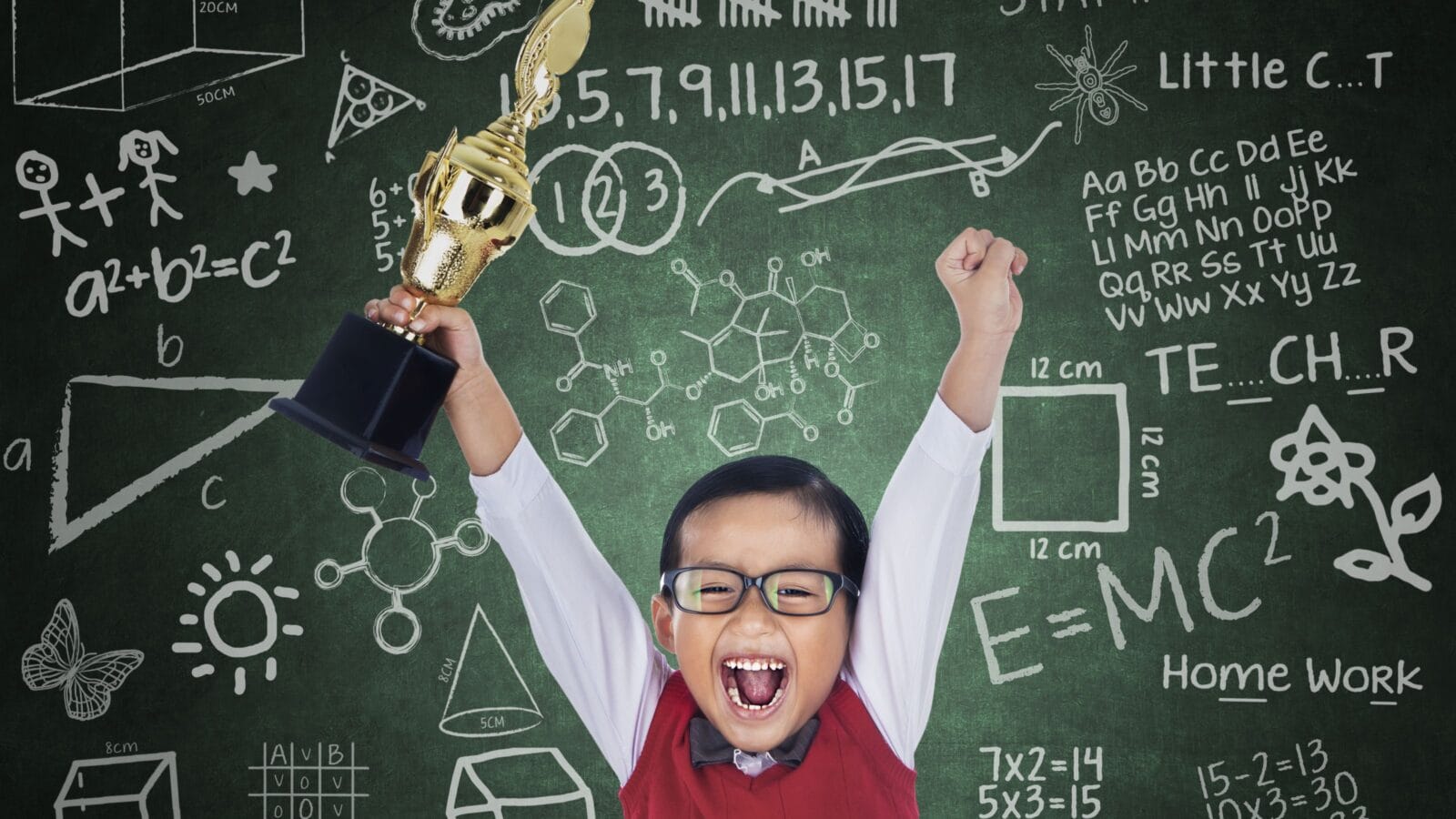 Happy student boy shouting while holding a trophy in classroom