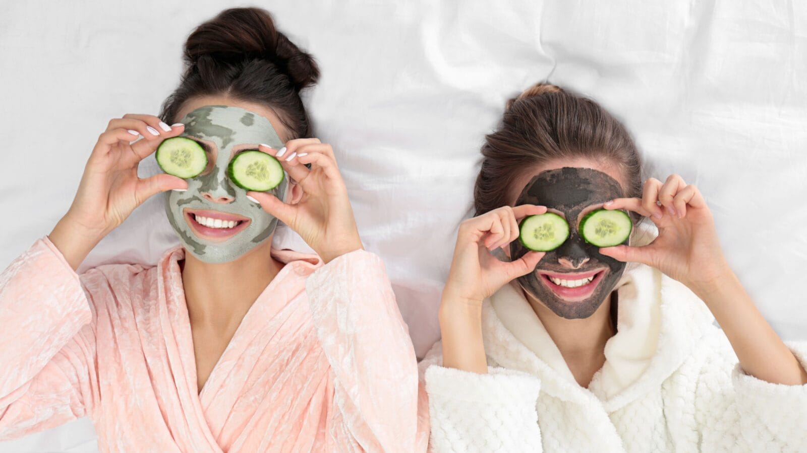Young friends with facial masks having fun on bed at pamper party