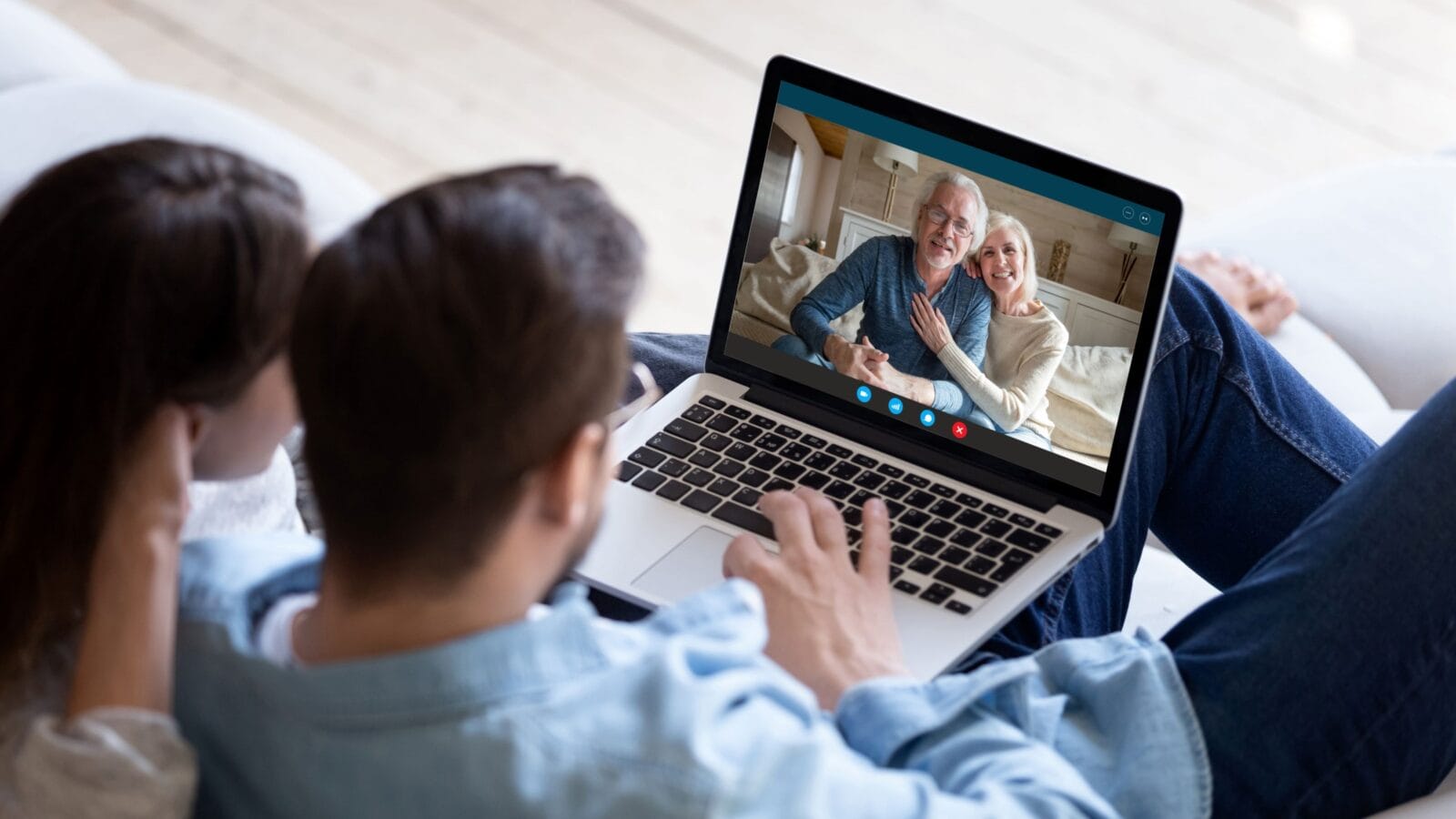 Couple communicating with elderly parents living abroad using computer and videocall application, laptop screen view over spouse shoulder