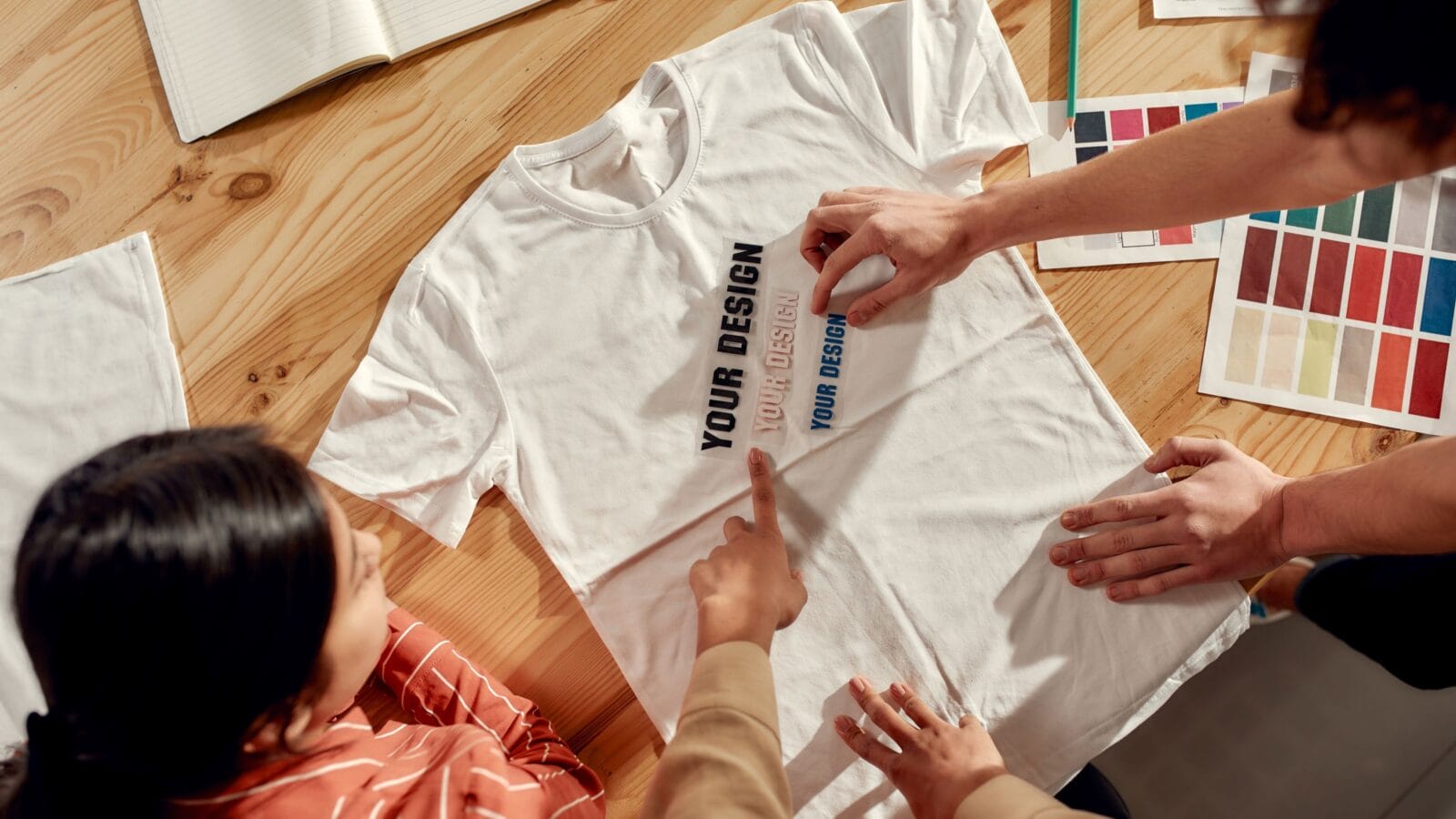 Top view of creative people trying on stickers with text, while discussing logo and design of T-shirt