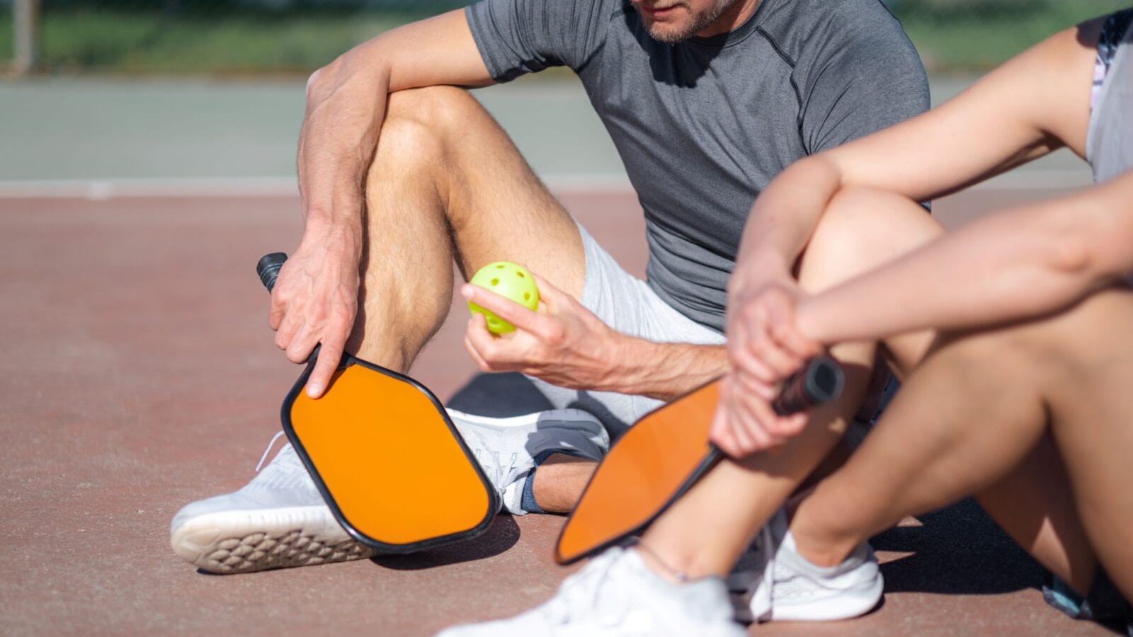 Pickleball game, relaxing pickleball players couple with yellow ball with paddle sitting after game