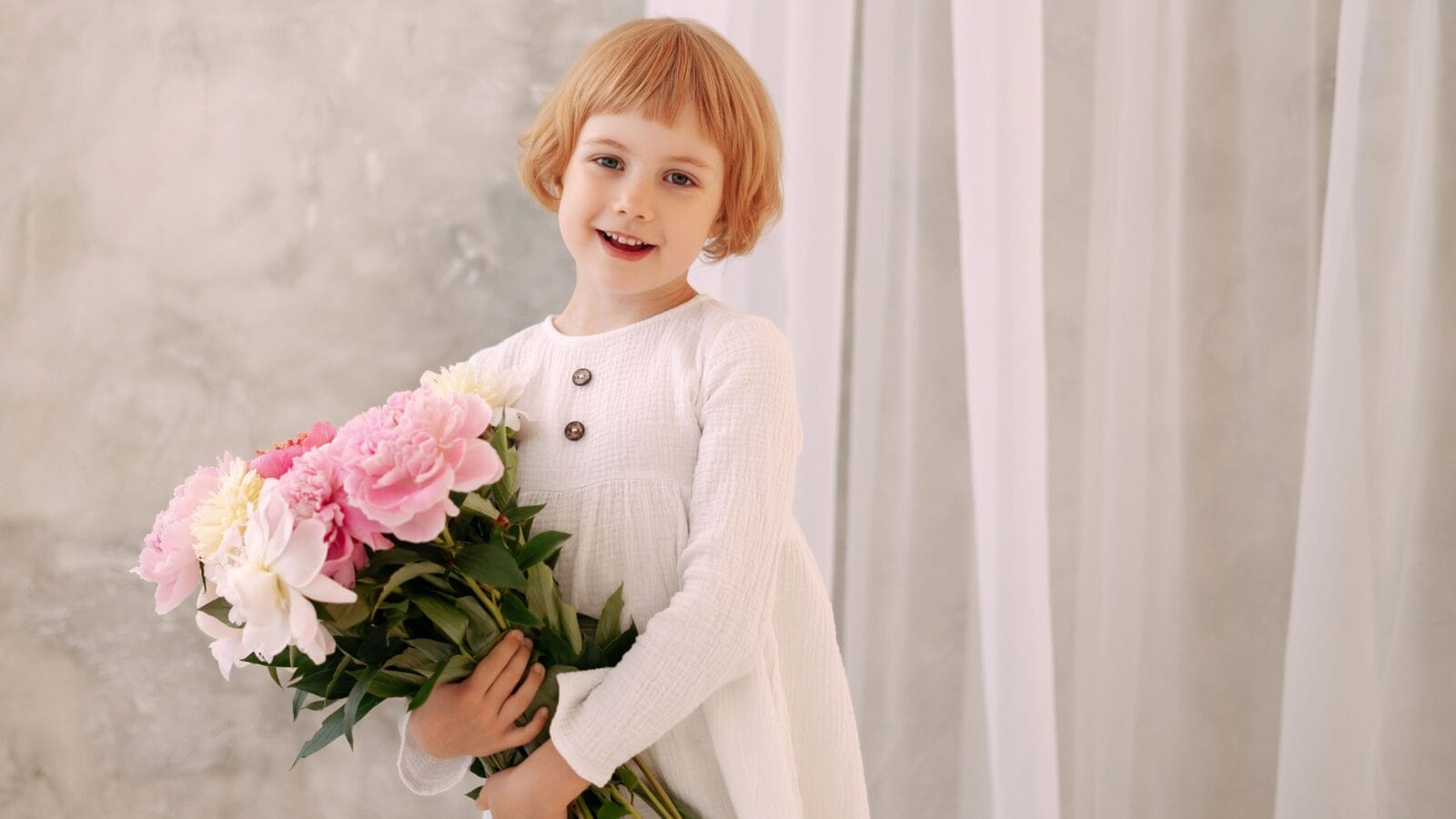 Child Blond 6-7 years old in a white dress holds a large bouquet of pale pink flowers in her hand