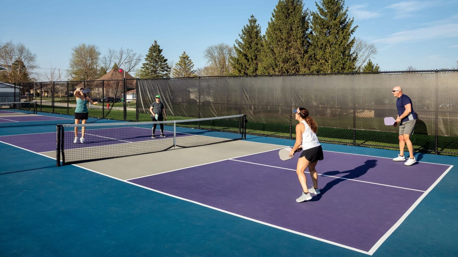 A female pickleball player returns a high volley at the net as her opponents prepare to return the ball on a dedicated court at a public park