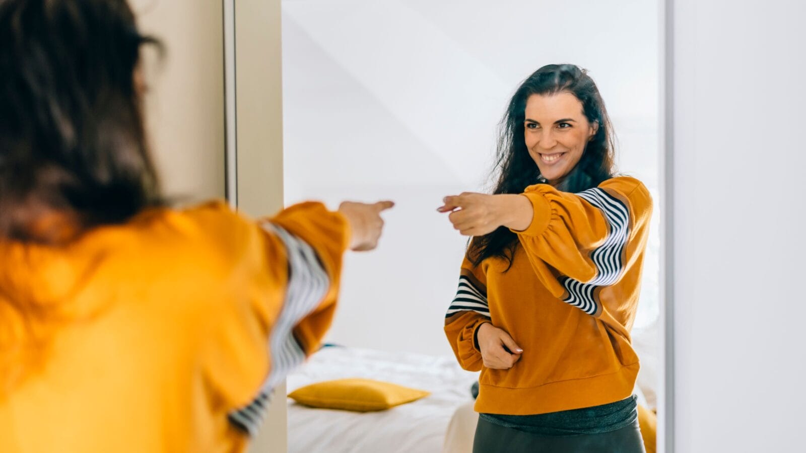 Self confident single woman pointing finger at reflection in mirror dancing and felling good
