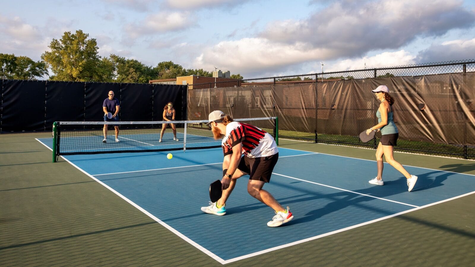 Four pickleball players rally against each other with two at the net ready to return a drive on a dedicated court