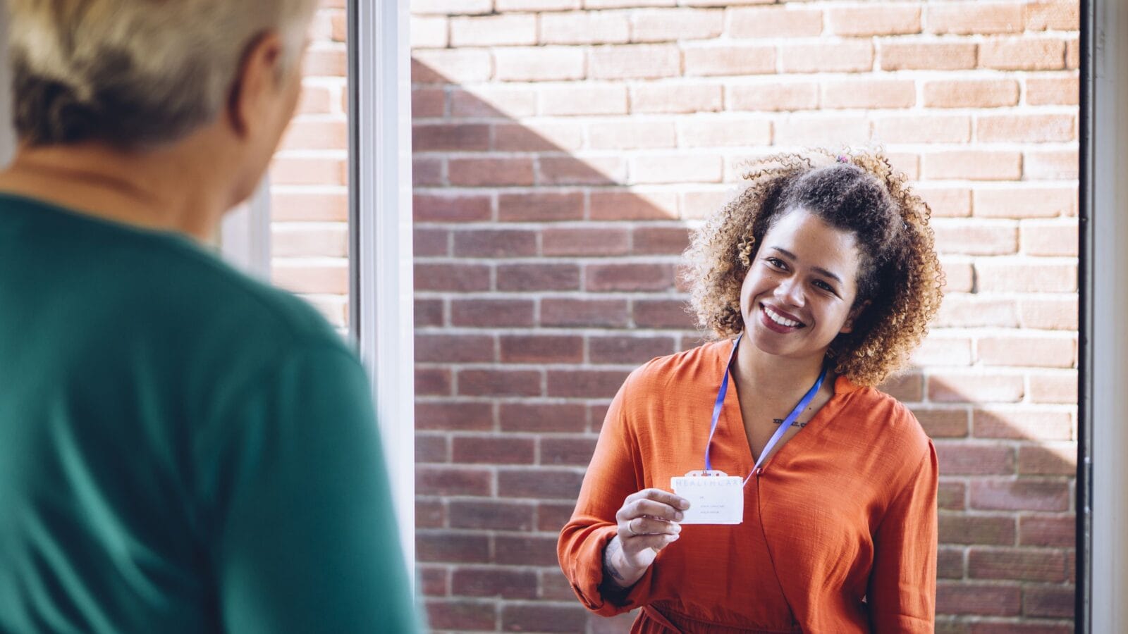 Healthcare worker showing her badge at the front door of a senior woman home
