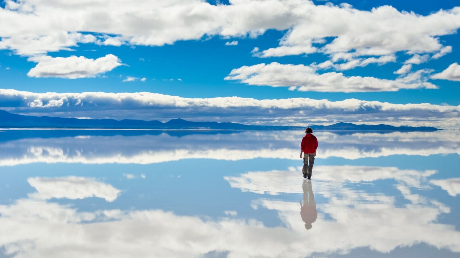 Girl in red on Salar de Uyuni in Bolivia covered with water with cloudy sky reflections