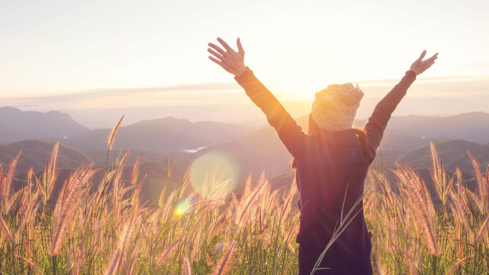 Carefree Happy Woman Enjoying Nature on grass meadow on top of mountain cliff with sunrise