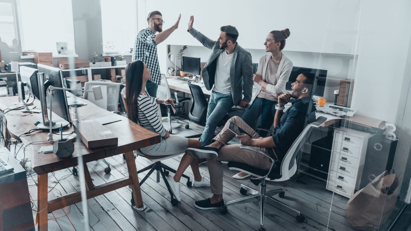 High-five for success! Two cheerful young business people giving high-five while their colleagues looking at them and smiling
