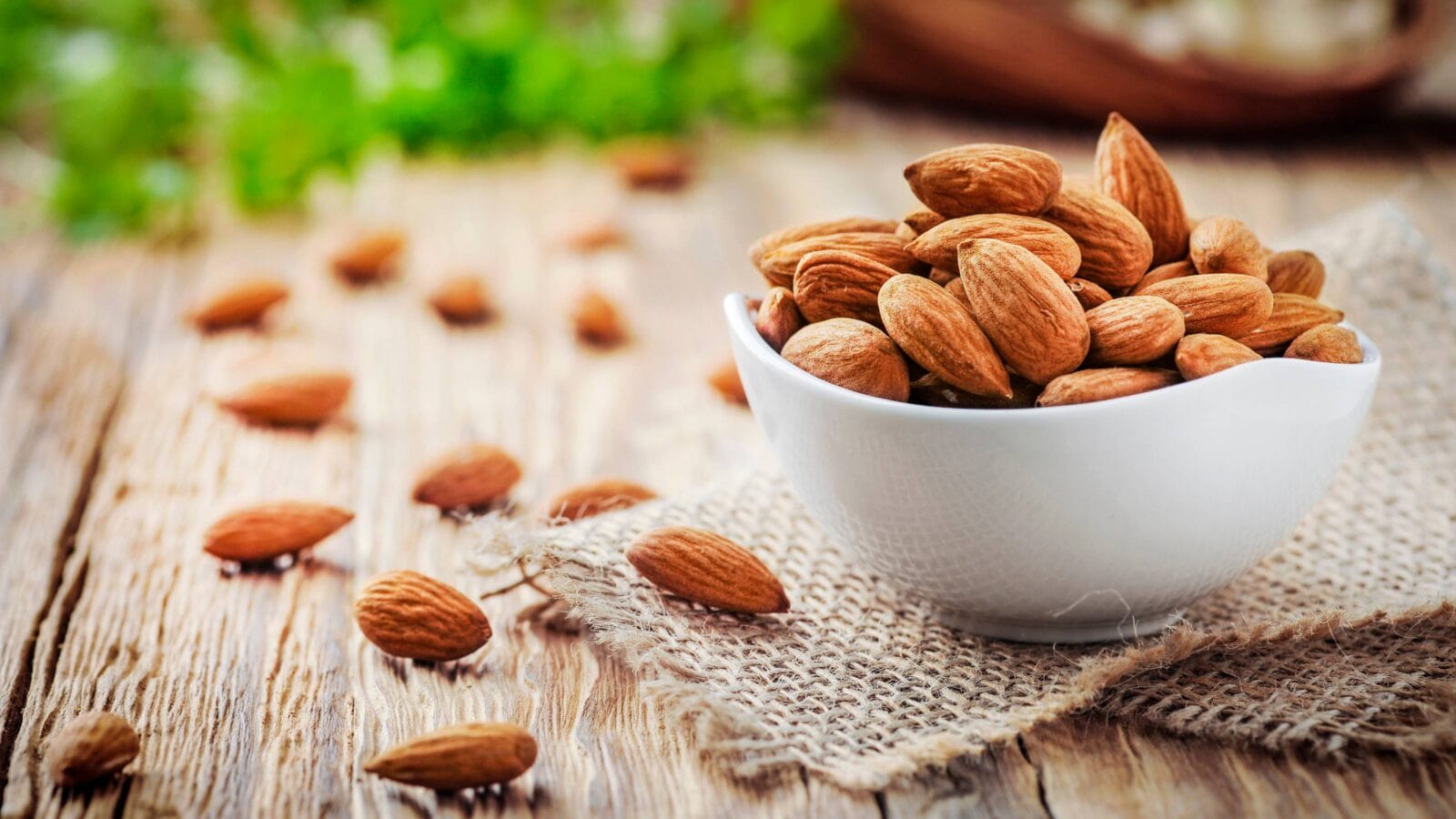 Almonds in white porcelain bowl on wooden table.