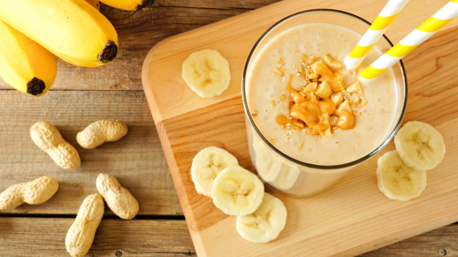 Peanut butter banana oat smoothie with paper straws, on a wood board on rustic table