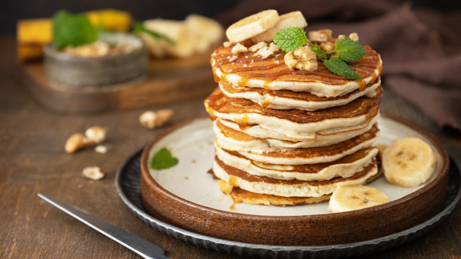 Delicious homemade banana pancakes with nuts and caramel on rustic wooden table.