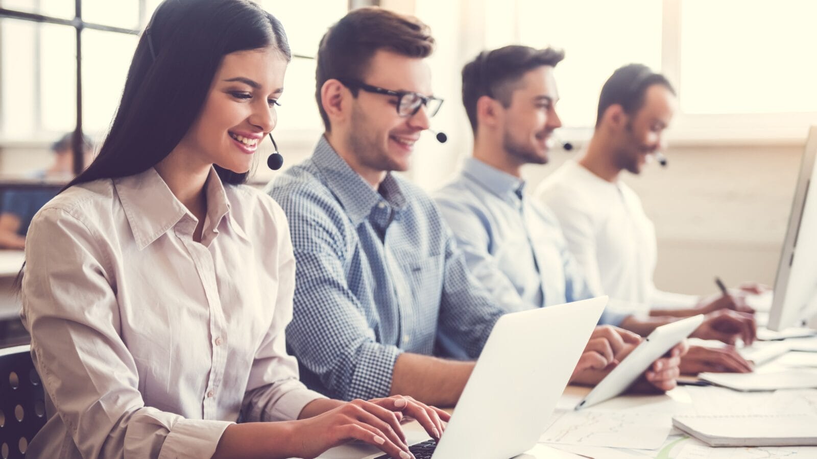Business people in headsets using computers and smiling.