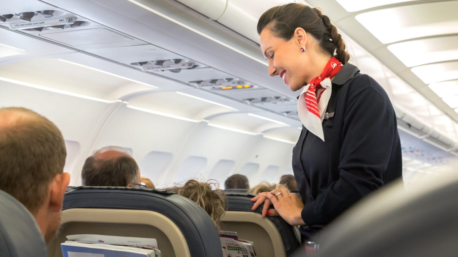 A female flight attendant is speaking with a passenger