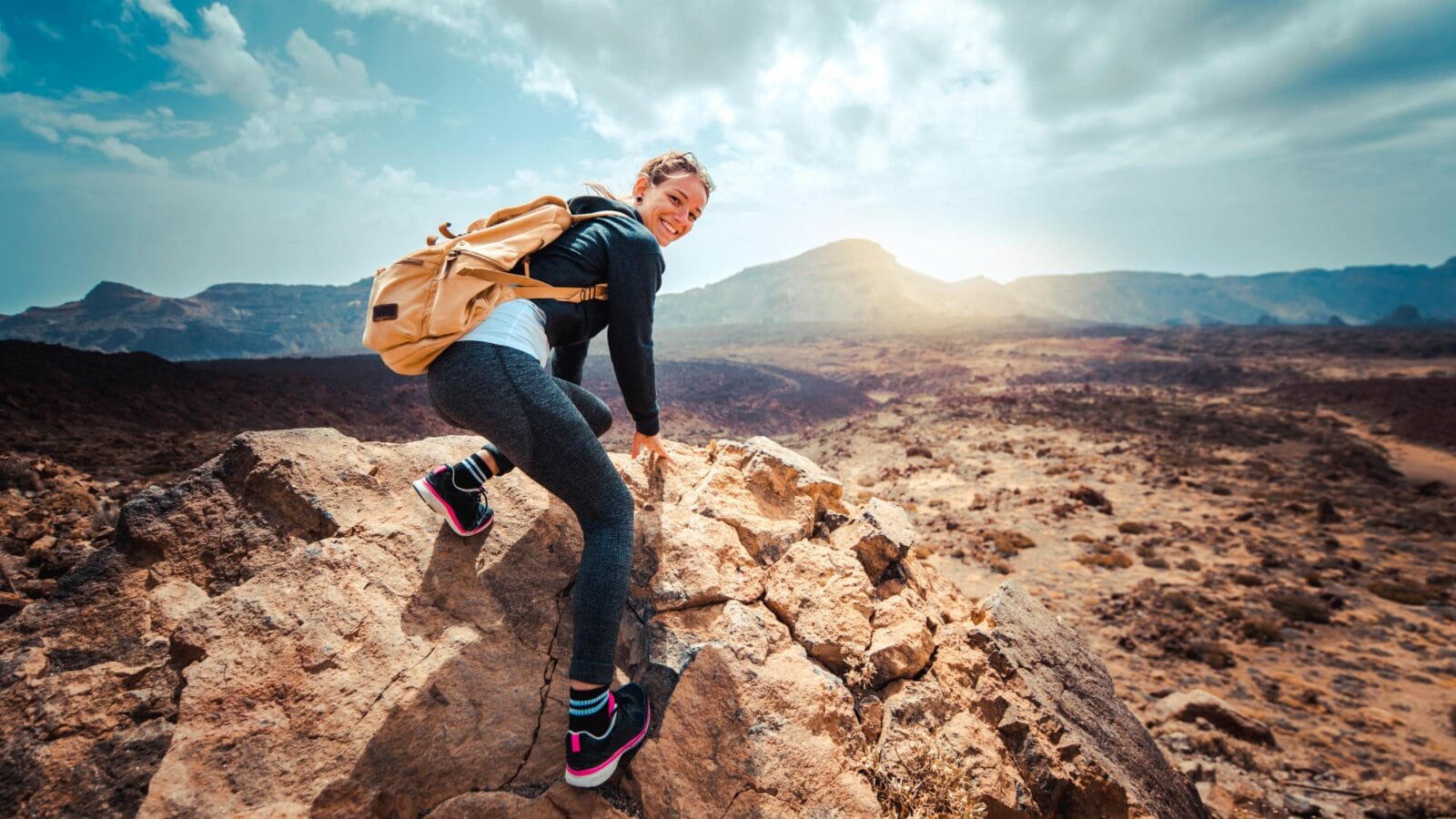 Portrait of a happy woman hiker standing on the top of mountain ridge against mountains