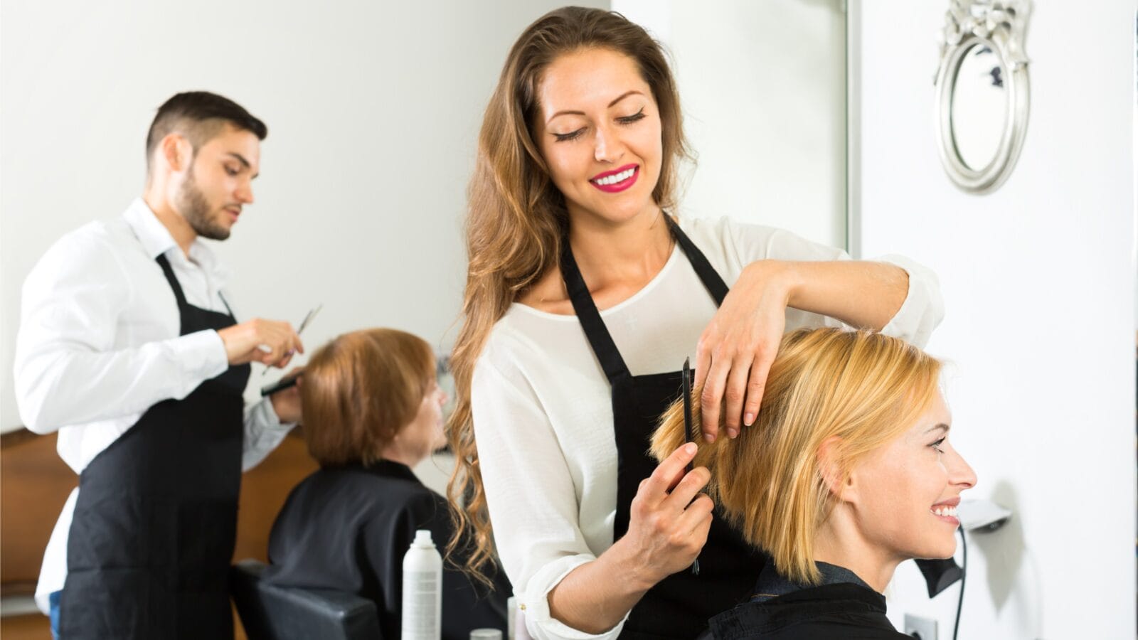 Smiling client sitting in a hair salon while hairdresser is combing her hair