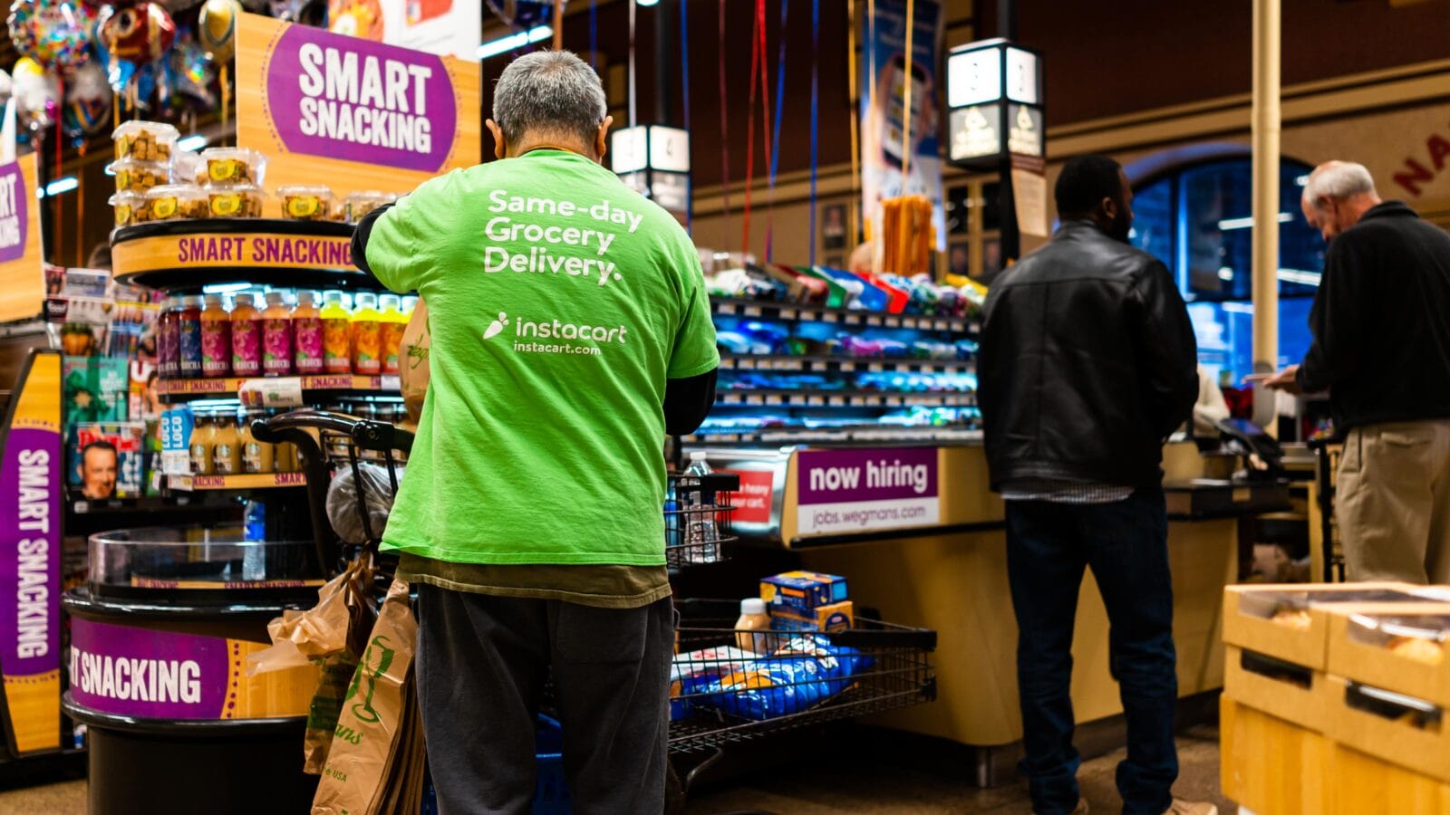 Wegmans grocery store interior with checkout counter and Instacart man worker and sign on shirt for same-day delivery