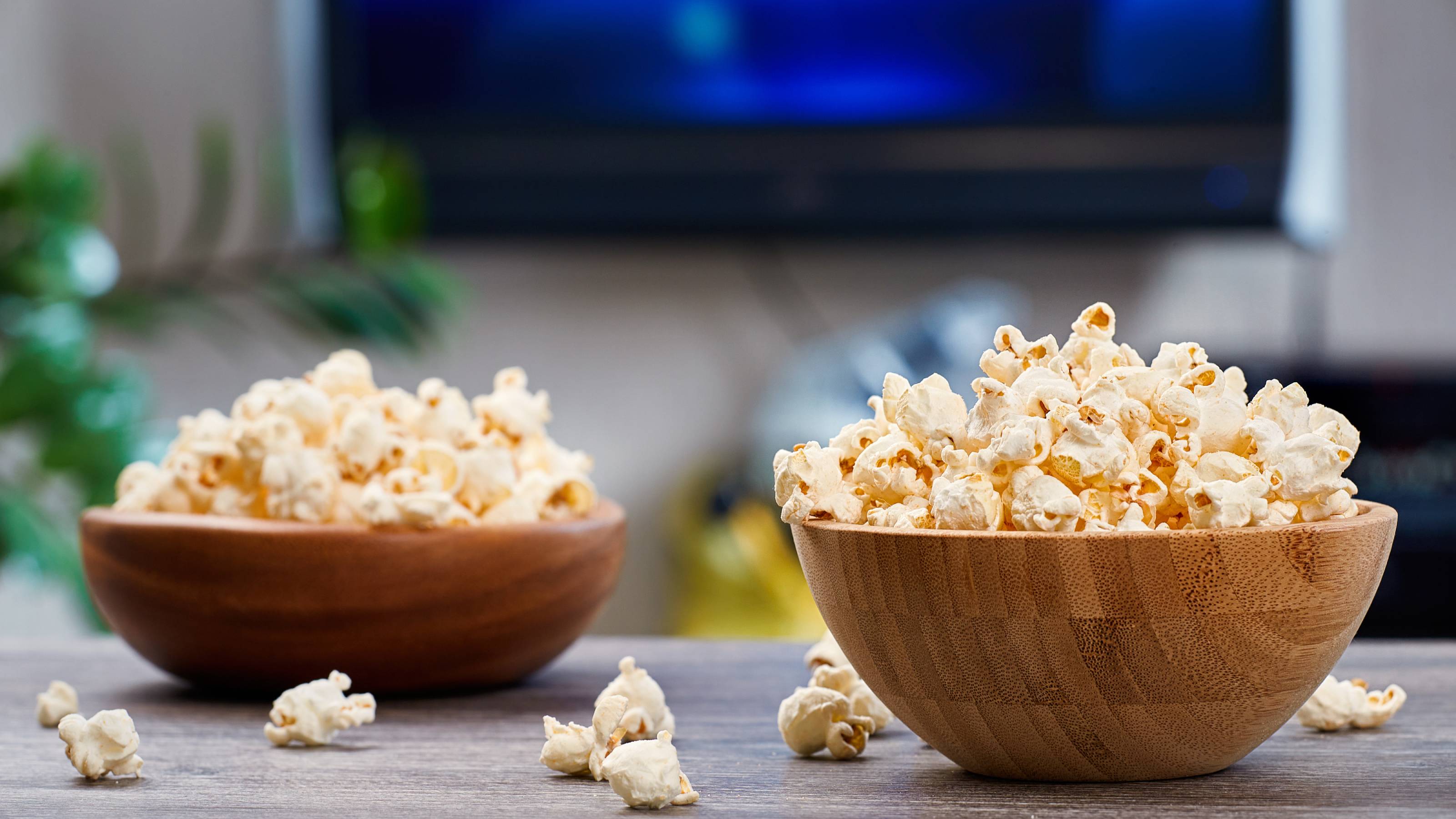 Two wooden bowls with fresh popcorn, on the background of a home interior with a TV.