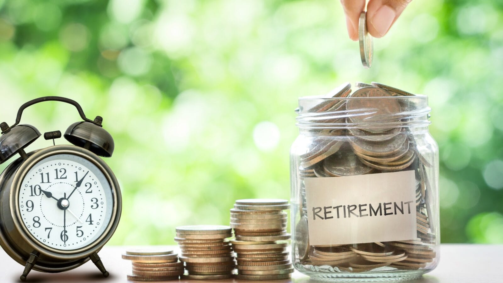 Hand putting Coins in glass jar for with retro alarm clock for time to money saving for retirement concept