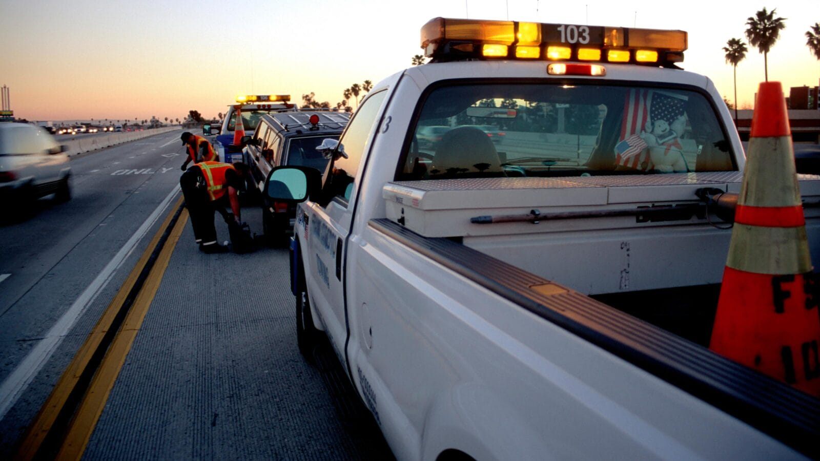 Municipal roadside assistance helping to tow away a broken car off the freeway at sunset